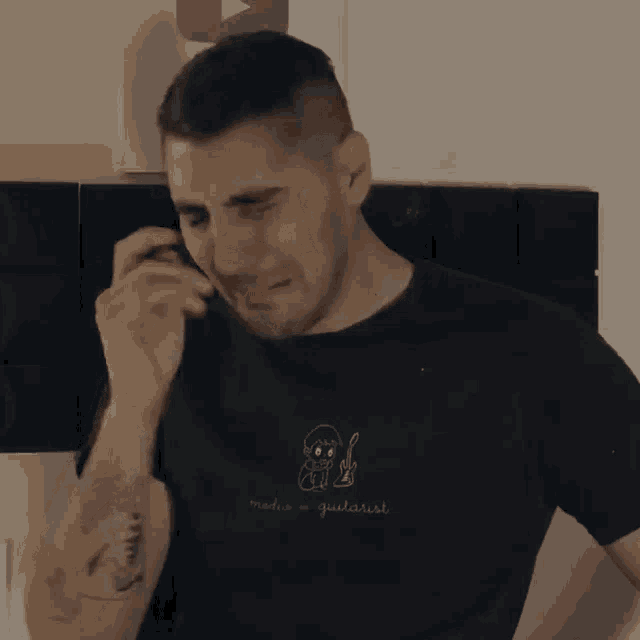 a man with a tattoo on his arm is crying while talking on a phone .