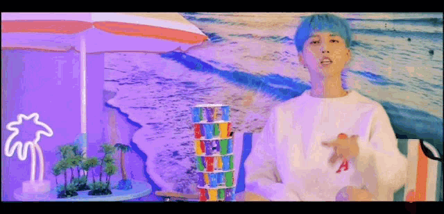 a man with blue hair is sitting at a table with a stack of cards and an umbrella .