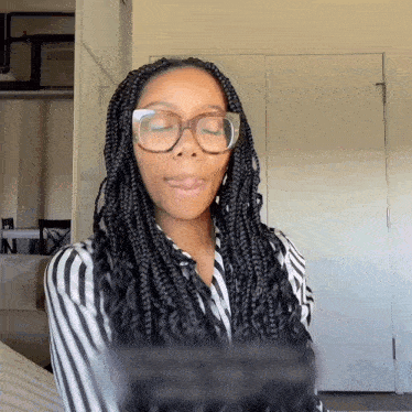 a woman with braids and glasses looks at the camera