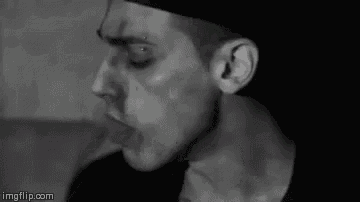 a black and white photo of a man smoking a cigarette in a room .