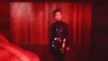 a woman in a black dress is standing in a dark room with a red light behind her .