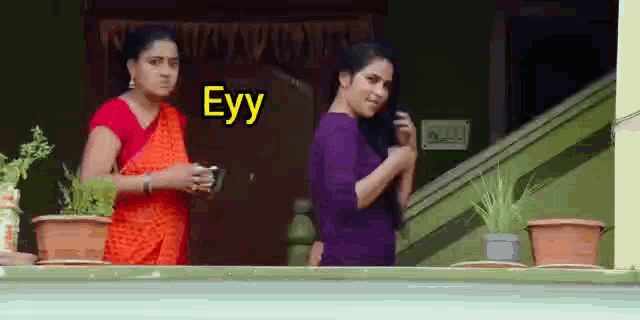 two women are standing next to each other on a balcony with a sign that says eyy on it .