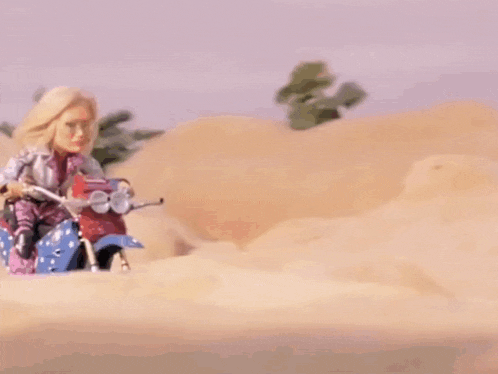 a doll is riding a scooter in the sand