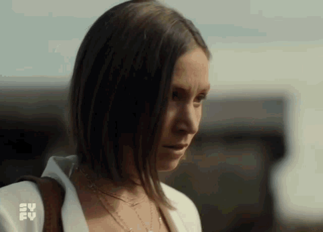 a woman with short hair is wearing a white shirt and a necklace and looking at the camera .