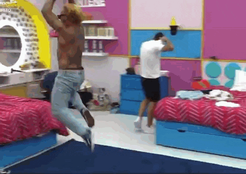 a shirtless man is jumping in the air in a bedroom with two beds