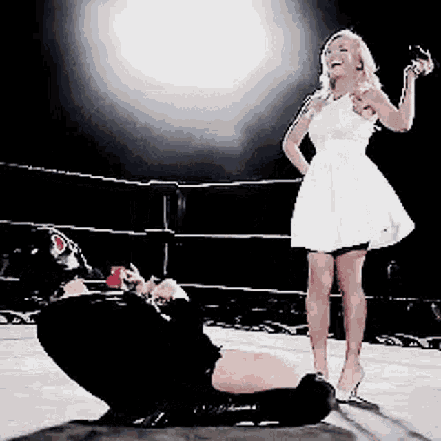 a woman in a white dress is standing next to a man in a wrestling ring holding a rose .