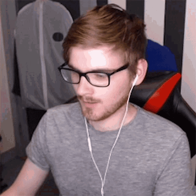 a man wearing glasses and ear buds looks at the camera