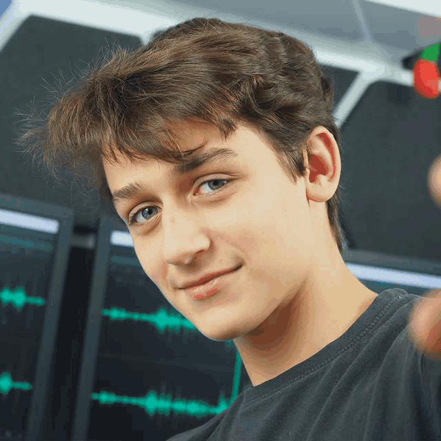 a young man in a black shirt is smiling in front of a computer screen