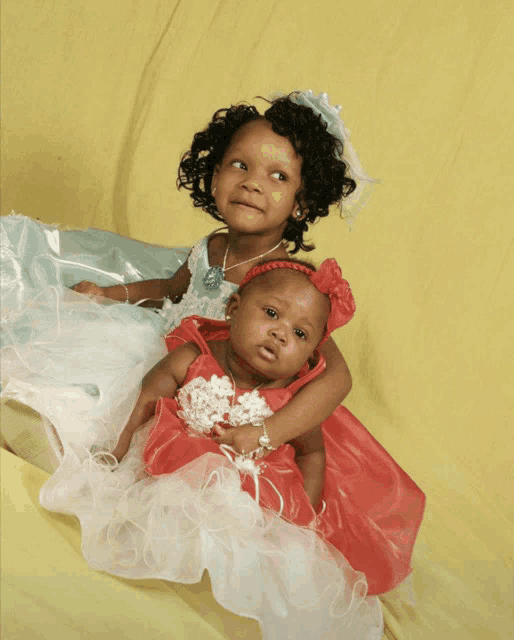 two little girls sitting next to each other wearing dresses