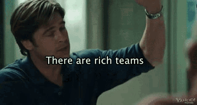 a man in a blue shirt is giving a high five with the words `` there are rich teams '' behind him .
