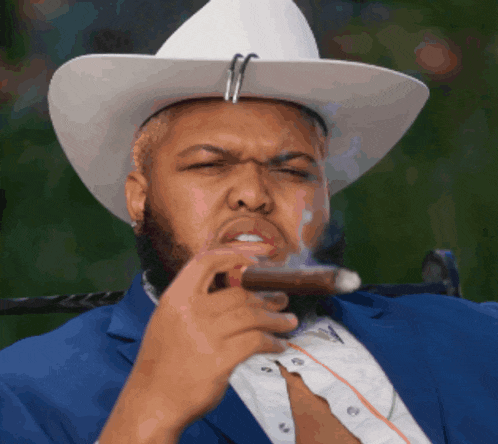 a man wearing a white cowboy hat and a blue suit is smoking a cigar
