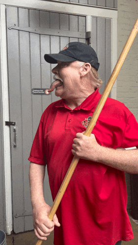 a man in a red shirt is holding a stick in his mouth