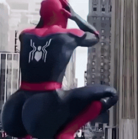 a man in a spiderman costume is squatting down in front of a building in a city .