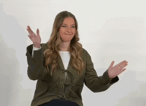 a woman in a green jacket is sitting down with her arms outstretched and making a funny face .