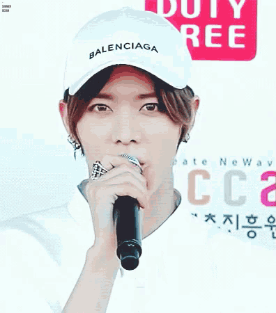 a young man wearing a white balenciaga hat is holding a microphone in his mouth .
