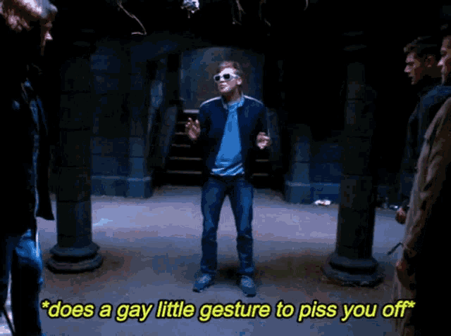 a man wearing sunglasses says " does a gay little gesture to piss you off " while standing in a dark room