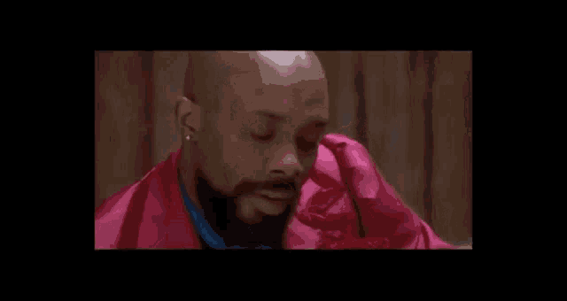 a bald man with a beard wearing a pink robe and smiling .