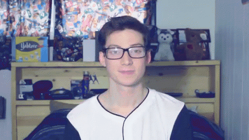 a young man wearing glasses stands in front of a shelf with a box of yankee tissues