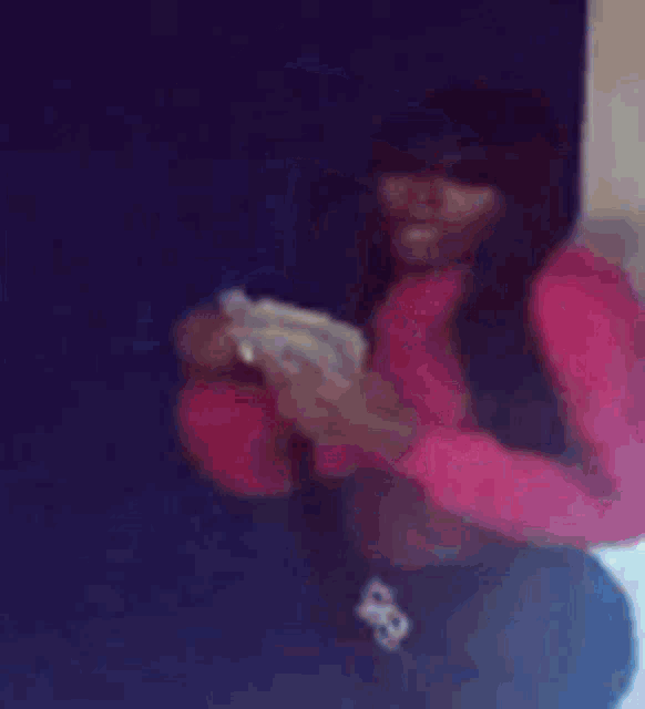 a woman in a pink sweater is holding a cell phone in her hand .