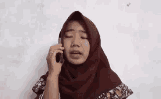 a woman in a hijab is talking on a cell phone and saying `` say , istiin aku pulsa '' .