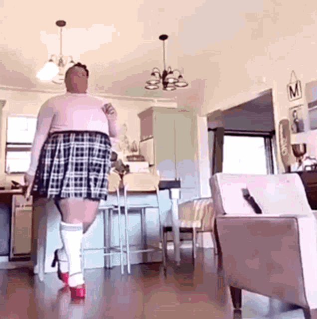 a woman wearing a plaid skirt and high heels is walking in a living room .