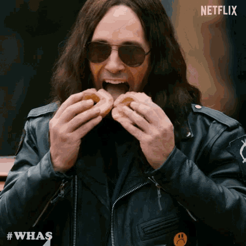 a man wearing sunglasses and a leather jacket is eating a donut with a netflix logo in the background