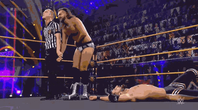 a referee holds up a shirtless wrestler 's arm in a wrestling ring with a wwe logo in the background
