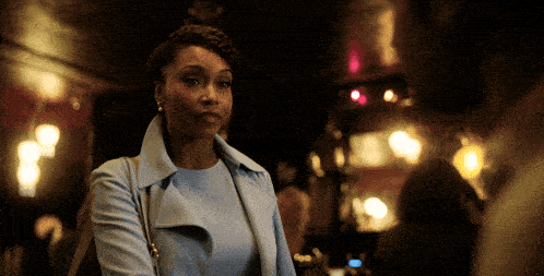 a woman wearing a light blue coat stands in a dark room