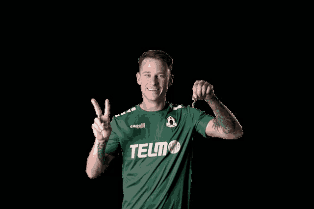 a man wearing a green shirt that says telmo giving a peace sign