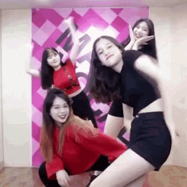 a group of young women are posing for a picture while dancing in front of a pink wall .
