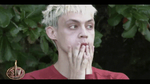 a man with blonde hair is covering his mouth with his hands while wearing a red shirt that says stv on it