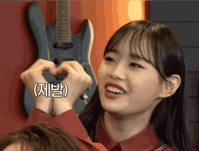 a woman is making a heart shape with her hands in front of a guitar