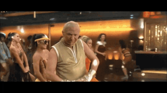 a man in a gold tank top is dancing in front of a crowd of women