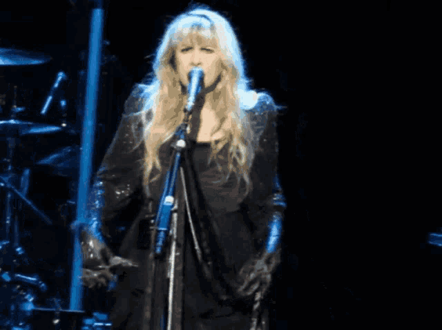 a blonde woman singing into a microphone with her arms outstretched