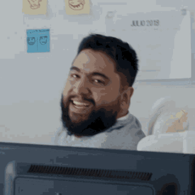 a man with a beard is smiling in front of a monitor