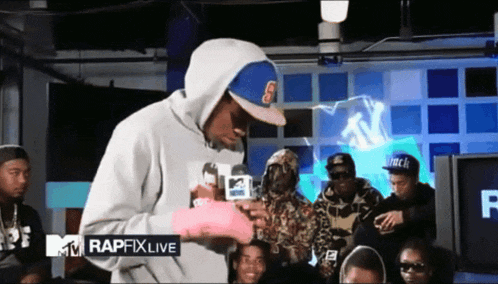 a man in a hooded sweatshirt stands in front of a rapfix live sign