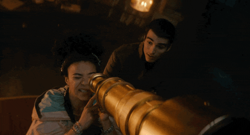a woman looks through a telescope while a man looks on