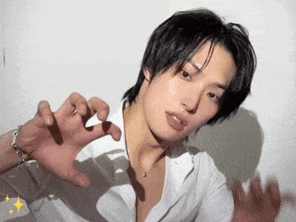 a young man wearing a white shirt and a necklace is making a cat face with his hands .