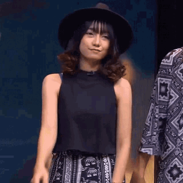 a woman wearing a hat and a black tank top stands next to a man wearing a patterned shirt