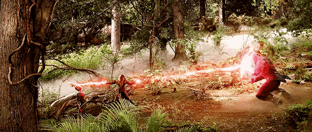 a man in a red suit is standing in the middle of a forest shooting a red light .