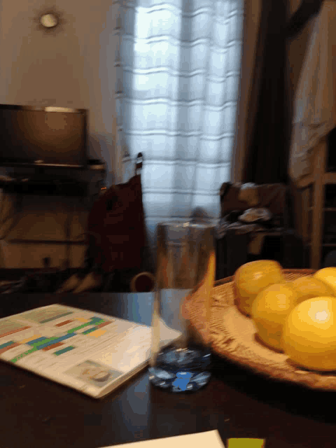a glass of water sits on a table next to a fruit bowl