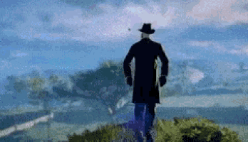 a man in a cowboy hat is standing on top of a grassy hill .