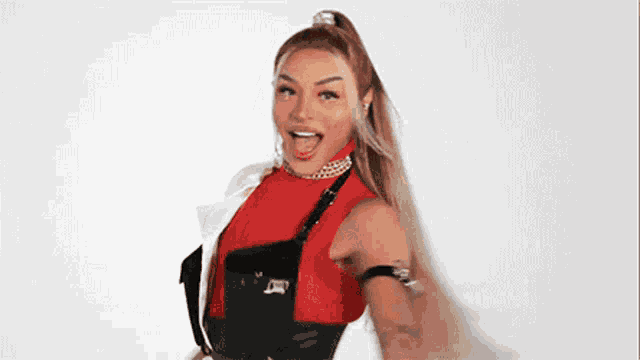 the woman is wearing a red top and black overalls and is dancing .