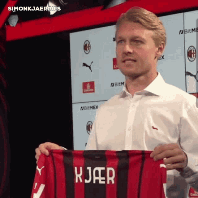 a man in a white shirt is holding up a red and black striped jersey with the name kjaer on it