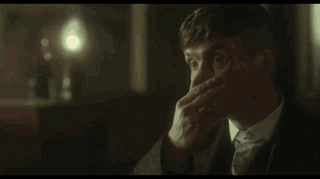 a man in a suit and tie is smoking a cigarette while sitting in a dark room .