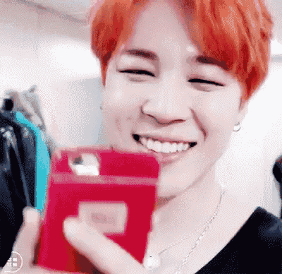 a man with red hair is smiling while holding a red cell phone in his hand .