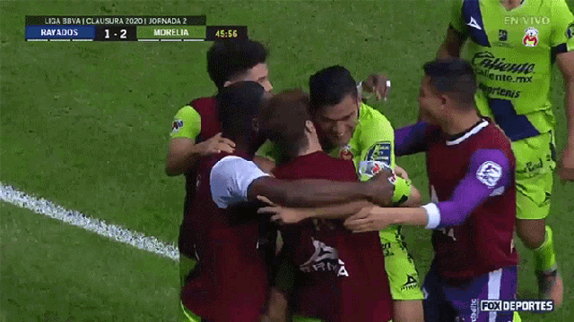 a group of soccer players huddle together on a field with a fox deportes advertisement in the background