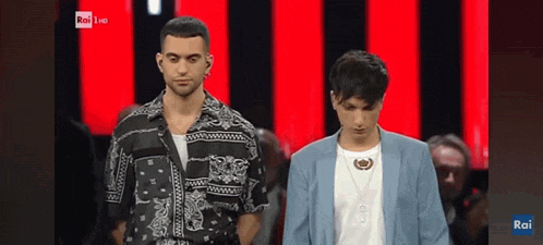 two men are standing next to each other in front of a red and black background . one of the men is wearing a blue jacket .