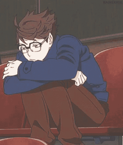a man with glasses is sitting on a red chair with his legs crossed