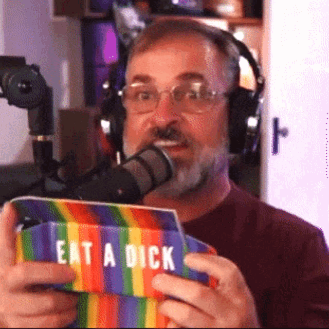 a man wearing headphones is holding a colorful sign that says eat a dick